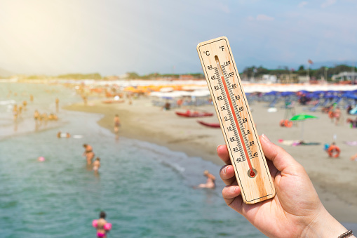 Woman hold a thermometer in front of a crowded Italian beach