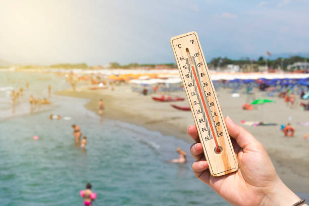 Woman hold a thermometer in front of a crowded Italian beach Woman hold a thermometer in front of a crowded Italian beach cristian stock pictures, royalty-free photos & images