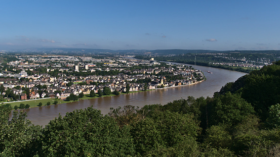 Beautiful aerial panoramic view of the northern part of city Koblenz, Rhineland-Palatinate, located on Rhine river, with flooded riverbank, houses and cargo vessel on sunny day with trees in front.