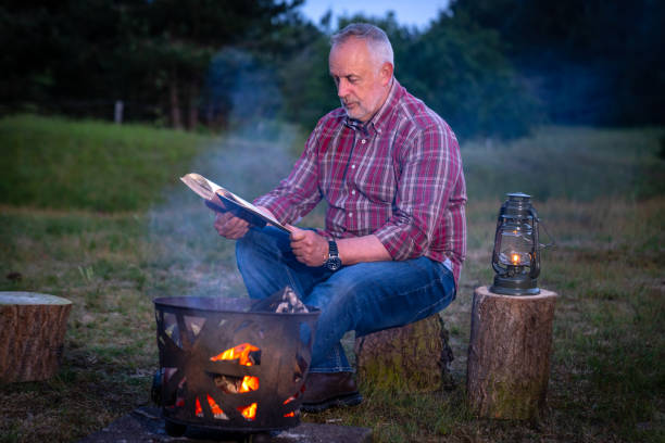 istock Senior man reading a book by the campfire 1330520641