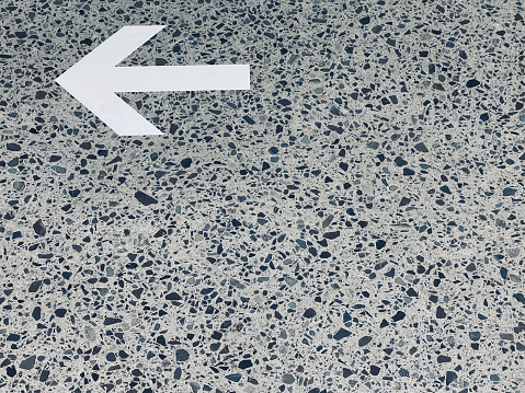 White arrow information sign showing to the left on a gray and black speckled floor