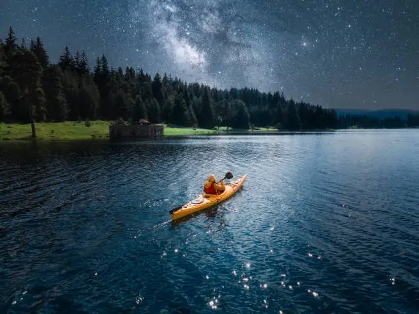 Photo of Woman kayaking in mountain lake under Milky way. Aerial view with starry sky. Paddling and ecotourism.