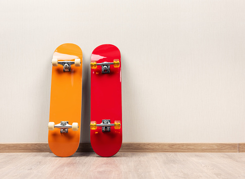 Two skateboards yellow and red stand upright against a wall on a wooden floor
