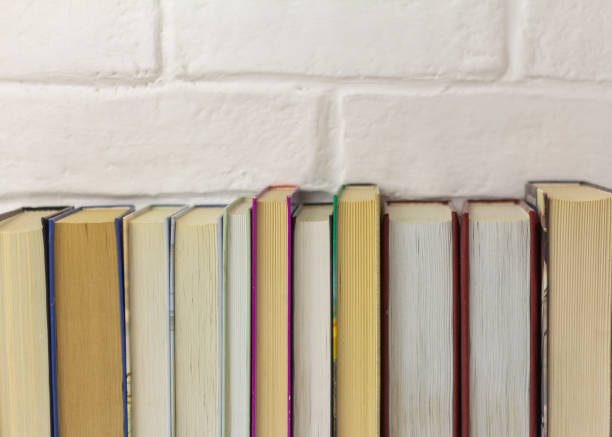 A collection of old books on a table or shelf against a brick wall.