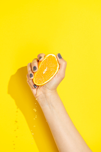 Hand holding, squeezing halved orange on yellow background