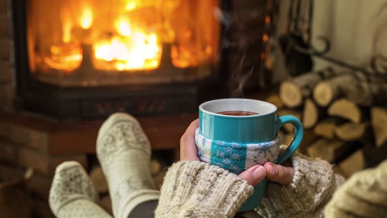 Warm atmosphere near the fireplace. In women's hands in a warm sweater, steam rises from a hot drink.