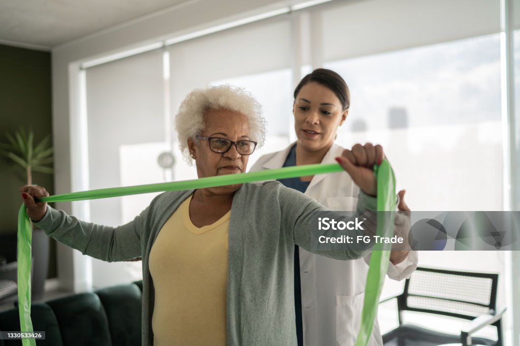 Physical therapist helping senior woman doing exercises with resistance band at home Physical Therapy Stock Photo