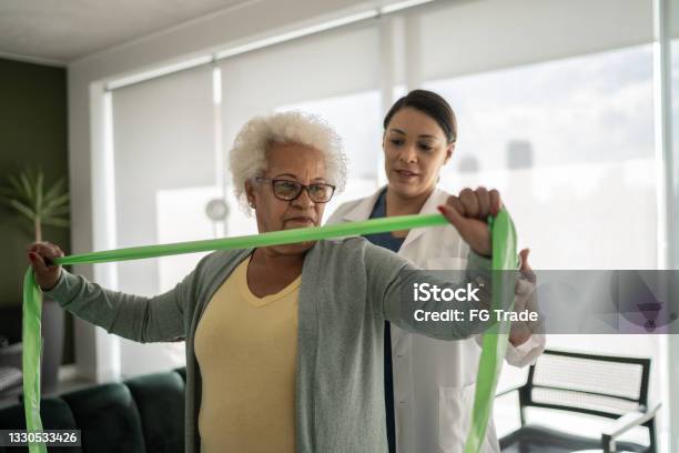 Physical Therapist Helping Senior Woman Doing Exercises With Resistance Band At Home Stock Photo - Download Image Now