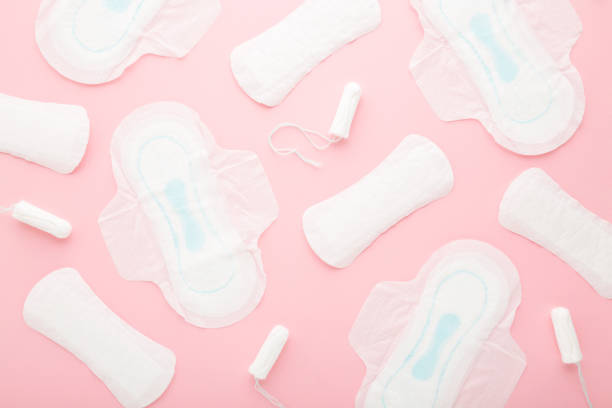 istock Opened white sanitary towels, tampons and panty liners on light pink table. Pattern background. Pastel color. Closeup. Different female hygiene products. Top down view. 1330540023