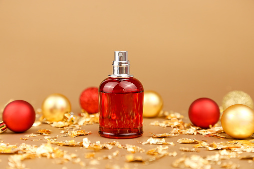 Unbranded Perfume spray red bottle, red and gold christmas balls and pieces of gold paper firecracker on golden background. Eau de toilette, front view, mockup. Home perfume