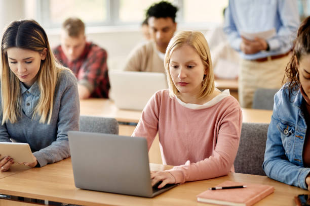 istock Young student using laptop while attending a class with her friends at university classroom. 1330545955