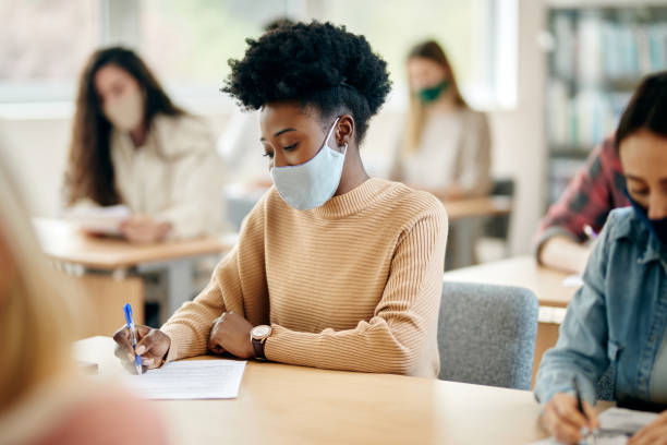 istock Black female student wearing face mask while writing an exam at the university during coronavirus pandemic. 1330546019
