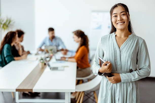 Doing business with a smile Confident young Asian businesswoman standing smiling at the camera in a boardroom with colleagues in the background central asian ethnicity stock pictures, royalty-free photos & images
