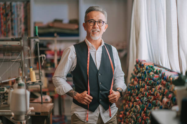 asian chinese senior tailor man with facial hair looking at camera smiling in atelier studio asian chinese senior tailor man with facial hair looking at camera smiling in atelier studio fashion designer photos stock pictures, royalty-free photos & images
