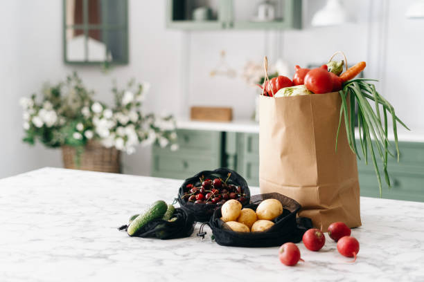 various vegetables in paper grocery and black mesh bags on kitchen island - matkasse bildbanksfoton och bilder