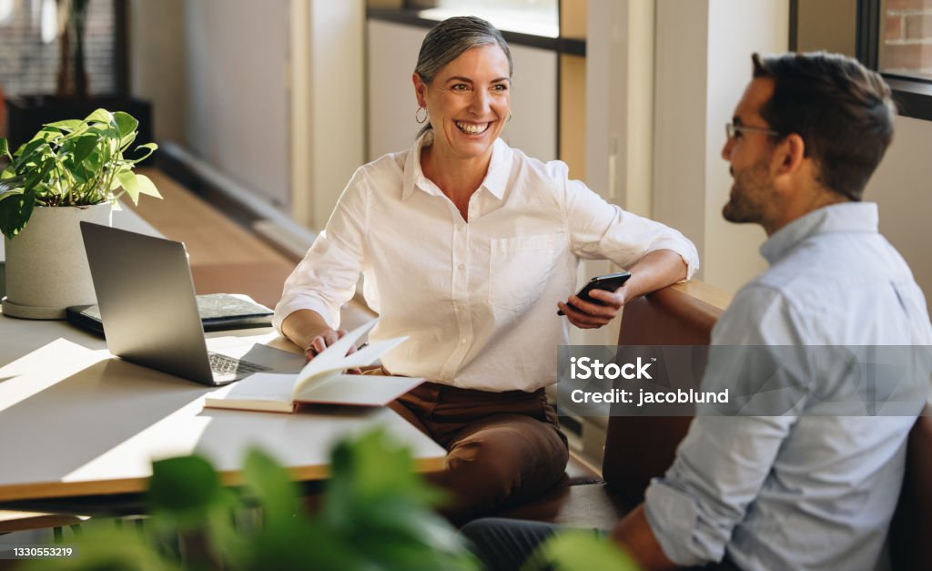 Senior businesswoman meeting with partner Businesswoman sitting at desk and explaining new project to coworker. Mature woman discussing working with partner in coworking office. Working Stock Photo