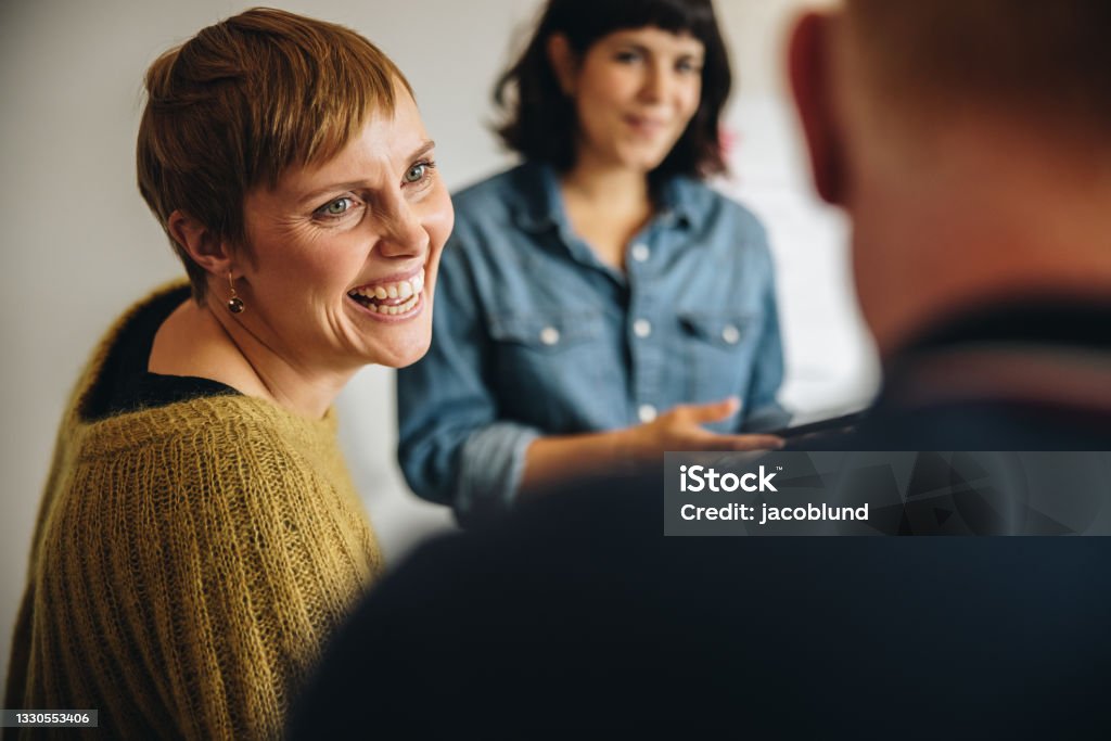 Businesswoman smiling during a meeting in office Businesswoman smiling during a meeting in office. Cheerful female professional looking at male colleague and smiling. Discussion Stock Photo