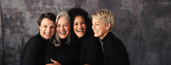 Smiling women of different ages standing together in studio. Group of four confident women embracing their natural and ageing bodies against a studio background.