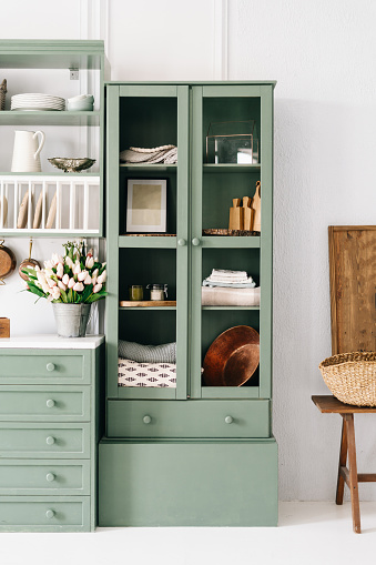 Vertical shot of tall green vintage cupboard with glass doors containing something different on each shelf, kitchen furniture with dishes and plates