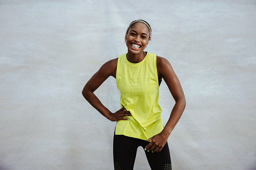 African woman in workout wear looking at camera and smiling. Fit woman athlete standing against white background.