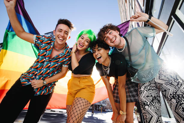 Young LGBTQ+ people celebrating pride Young LGBTQ+ people celebrating pride together. Group of young queer people smiling cheerfully while holding the rainbow pride flag. Four friends celebrating together at a gay pride parade. gay pride people stock pictures, royalty-free photos & images