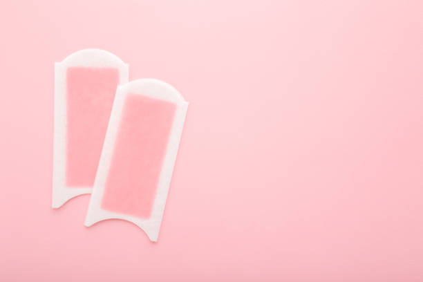 Two wax strips on light pink table background. Pastel color. Closeup. Female product for smooth body skin. Empty place for text. Top down view.