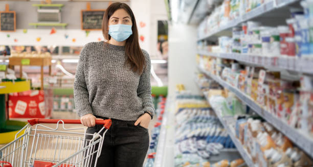 девушка в защитной маске стоит с тележкой для покупок возле холодильников с молочными продуктами в продуктовом супермаркете. - retail occupation flash стоковые фото и изображения