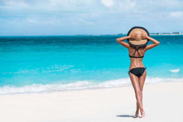 Summer vacation happiness carefree sun hat woman Summer vacation happiness carefree joyful woman standing on white sand enjoying tropical beach destination. Holiday bikini girl relaxing from behind holding straw hat on Caribbean vacation sea water. bathing suit stock pictures, royalty-free photos & images