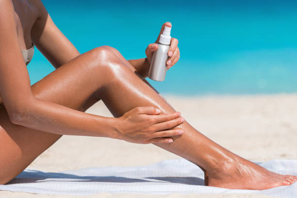 donna che spruzza crema solare crema solare lozione in spiaggia - abbronzatura foto e immagini stock