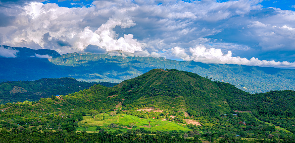 Panorama of the Andes Mountain range as viewed from the town of Anapoima in the Tequendama Province of the Department of Cundinamarca in Colombia, South America. Lush green trees and a lovely sky make for a splendid landscape. The clouds and sunlight also make interesting shadow patterns on the hills. Photo shot in the afternoon sunlight; horizontal format. Copy space. No people.