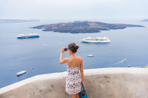 europa reise touristin, die mit dem telefon fotost vom mittelmeer in santorini, oia, griechenland, mit kreuzfahrtschiffen, die im meereshintergrund segeln - hat oia europe vacations stock-fotos und bilder