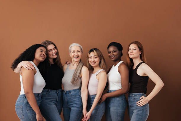 multi-ethnic group of women of different ages posing against brown background looking at camera - woman stockfoto's en -beelden