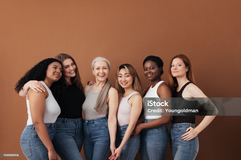 Multi-ethnic group of women of different ages posing against brown background looking at camera Women Stock Photo