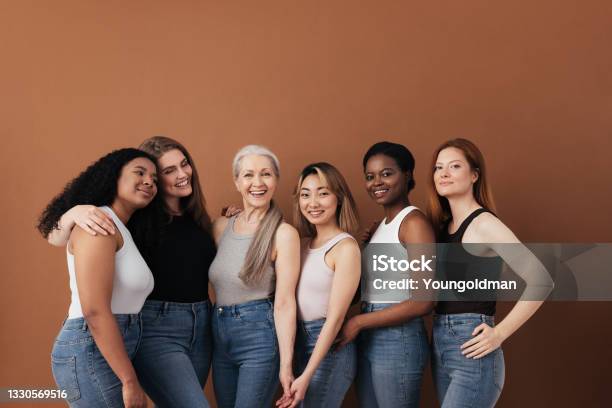 Multiethnic Group Of Women Of Different Ages Posing Against Brown Background Looking At Camera Stock Photo - Download Image Now