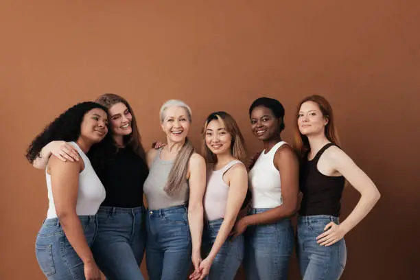 Photo of Multi-ethnic group of women of different ages posing against brown background looking at camera