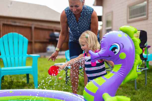 bambina bambina che gioca con la famiglia mista di gruppi etnici nella serie di foto divertimento summer time summer time in back yard kiddie - splashing color image front view head and shoulders foto e immagini stock