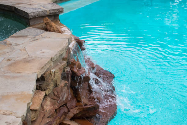 Waterfall over rocks from hot tub on higher level down to swimming pool -Refreshing and cool on a summer day stock photo