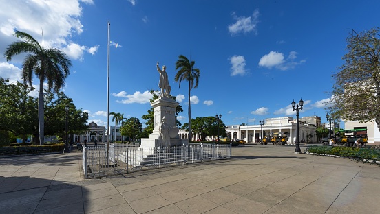 Cienfuegos, Cuba, December 3, 2017: View of the José Martí Park in the city center. The park bears the name of the Cuban revolutionary philosopher and political theorist José Martí whose statue is seen in the center of the square. In the background is the Arch of Triumph dedicated to Cuban independence. The historic center of Cienfuegos is listed as UNESCO World Heritage Site.