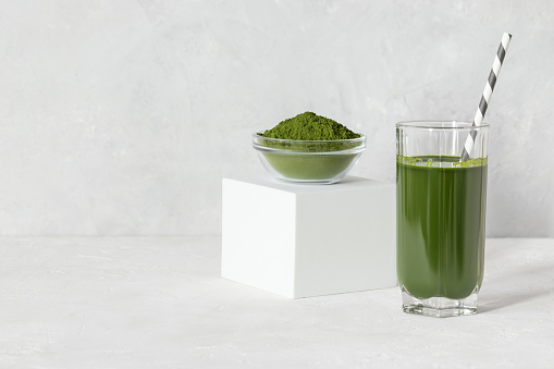 Green drink with chlorella in a glass and powder on a white concrete background. Healthy detox drink. Superfood concept. Space for text.