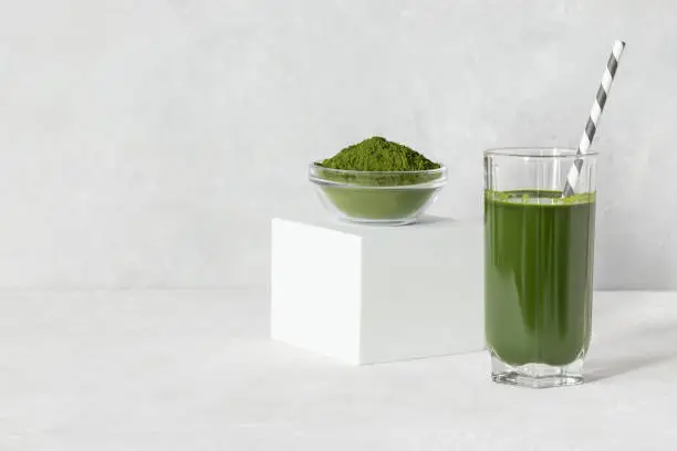 Green drink with chlorella in a glass and powder on a white concrete background. Healthy detox drink. Superfood concept. Space for text.