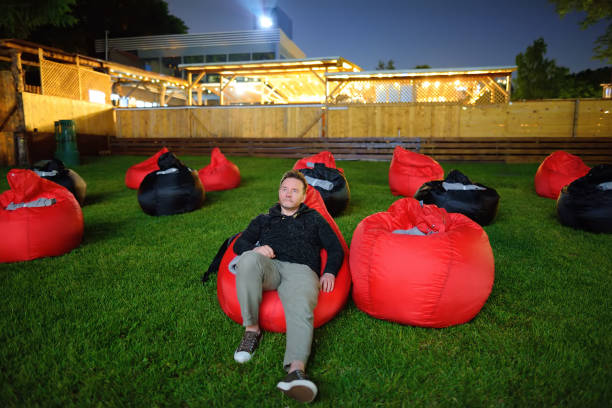 homem bonito deitado no travesseiro na grama e assistindo filme no cinema ao ar livre em parque público. passar a noite perfeita ou o fim de semana ao ar livre. lazer e entretenimento para as pessoas no verão. - night in the city - fotografias e filmes do acervo