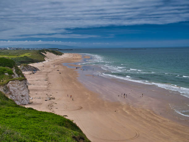 le sable immaculé de whiterocks beach et les falaises côtières sur la côte d’antrim causeway en irlande du nord, au royaume-uni. pris par une journée ensoleillée en été avec des nuages légers et un ciel bleu. - portrush photos et images de collection