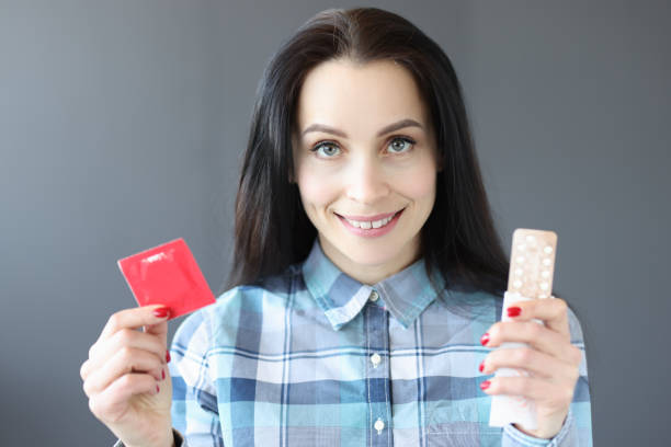 femme brune tenant un condom et des pilules contraceptives - contraceptive sex education birth control pill condom photos et images de collection