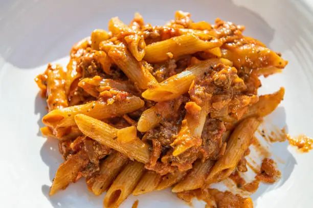 Closeup flat top lay view of fresh red tomato sauce marinara and ground lamb or beef bolognaise with penne pasta noodles on white plate background
