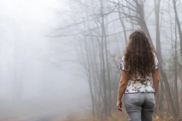 Back of young woman hiker on Cedar Cliffs forest woods trail in Wintergreen Resort, Virginia standing looking at view in morning fog foggy weather trees
