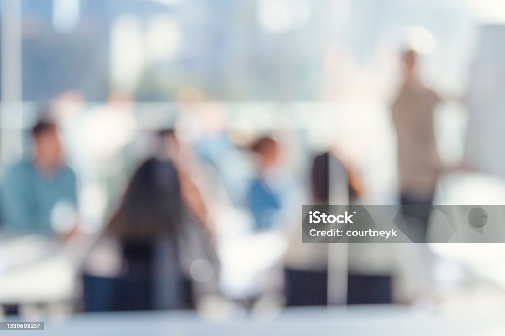 Defocussed image of Business people watching a presentation. Defocussed image of Business people watching a presentation. A mature man is writing on the whiteboard with charts and graphs. They are sitting in a board room, All are casually dressed. Defocused Stock Photo