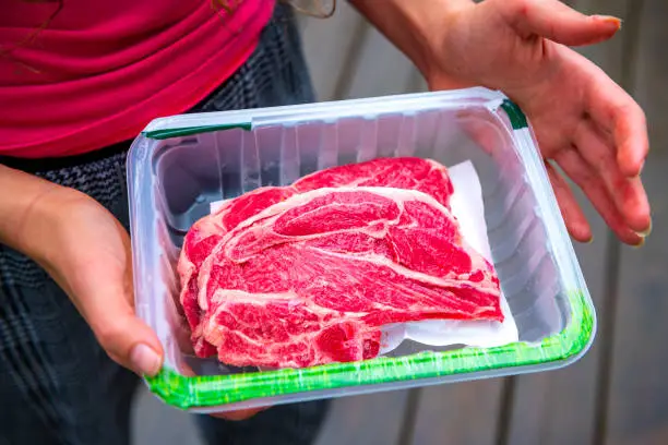 Photo of Red raw lamb meat shoulder chops from New Zealand packaged storebought with woman holding open plastic container showing