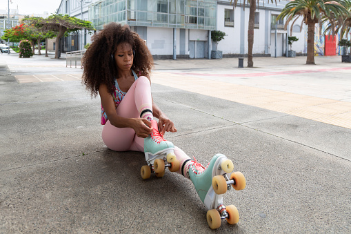 young Afro skater woman seated tying her skates