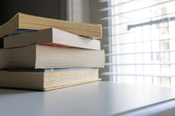 A stack of books sitting on a table with natural light filtering through the window.