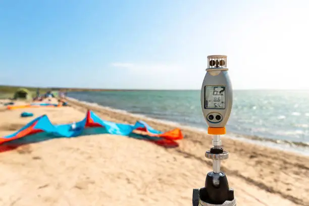 Close-up anemometer wind meter gadget against surf kite equipment on sand beach shore watersport spot on bright sunny day surfing tent campsite sea ocean coast. Fun adventure travel sport acitivity.